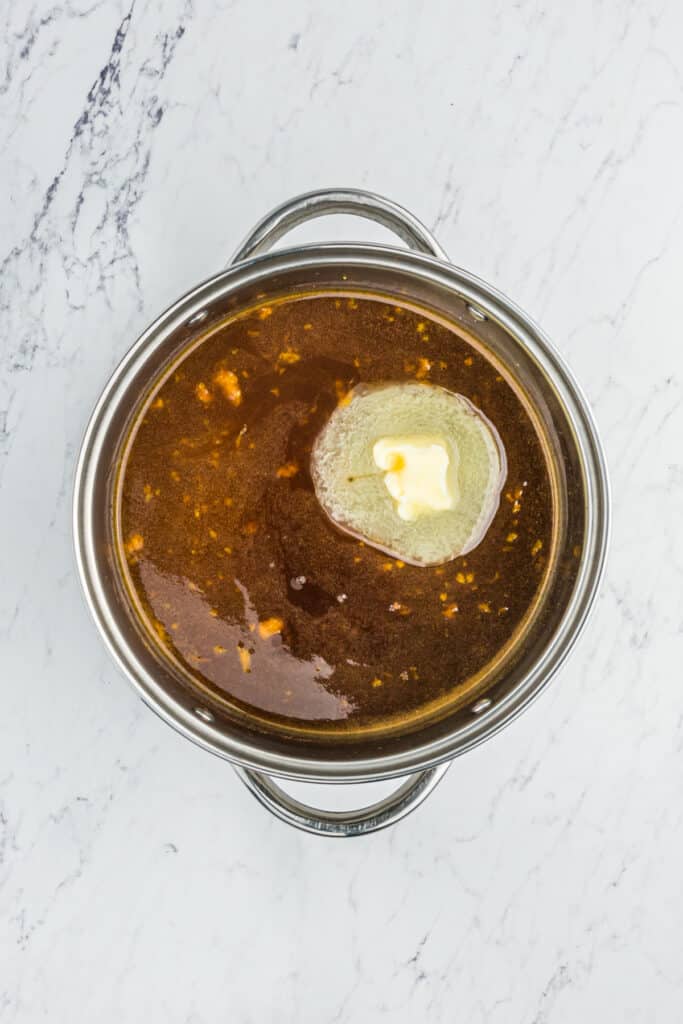 A saucepan of brown sugar, orange juice, spices and butter melting into syrup.