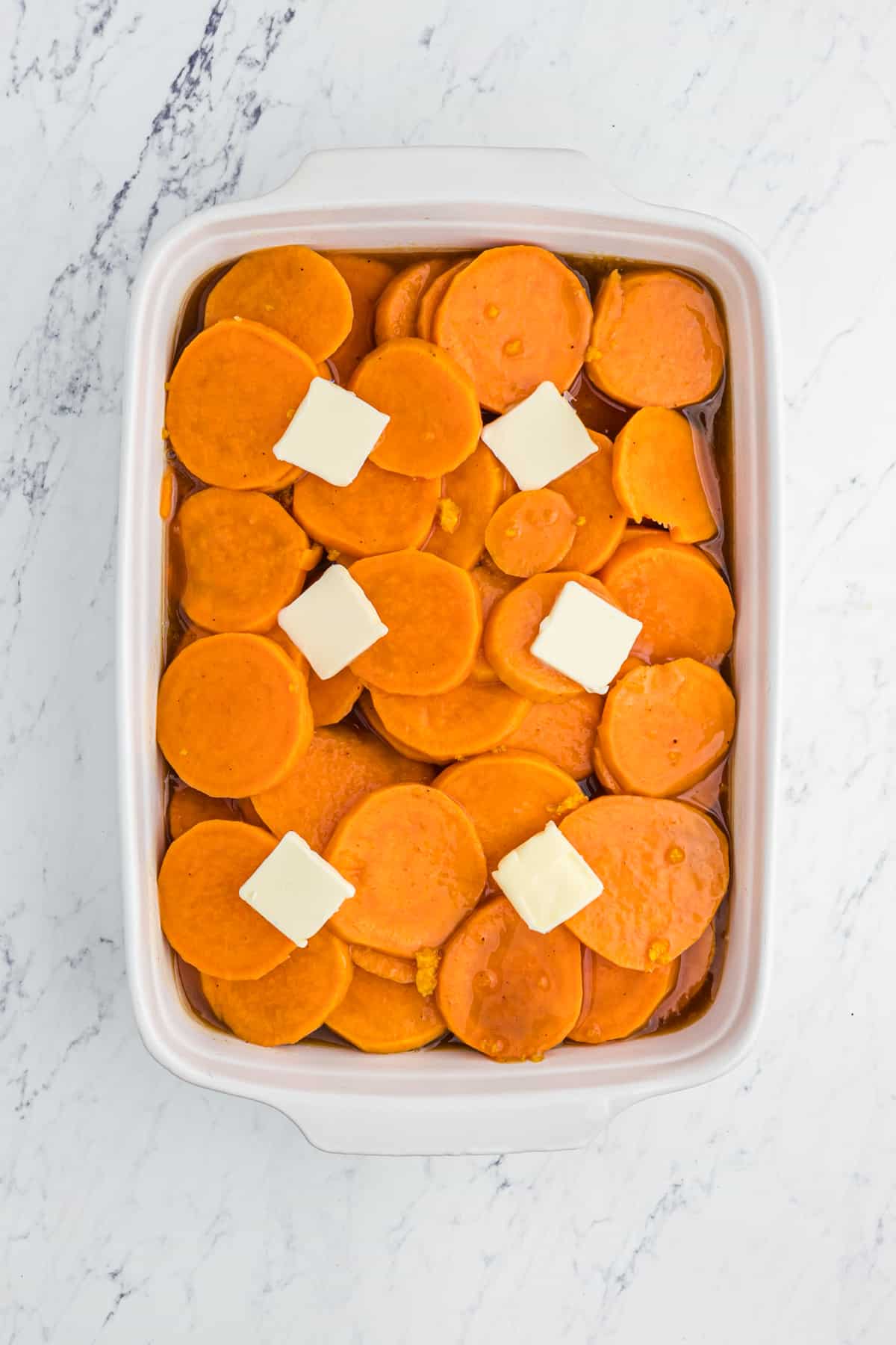 Sliced yams in a white baking dish topped with pats of butter.