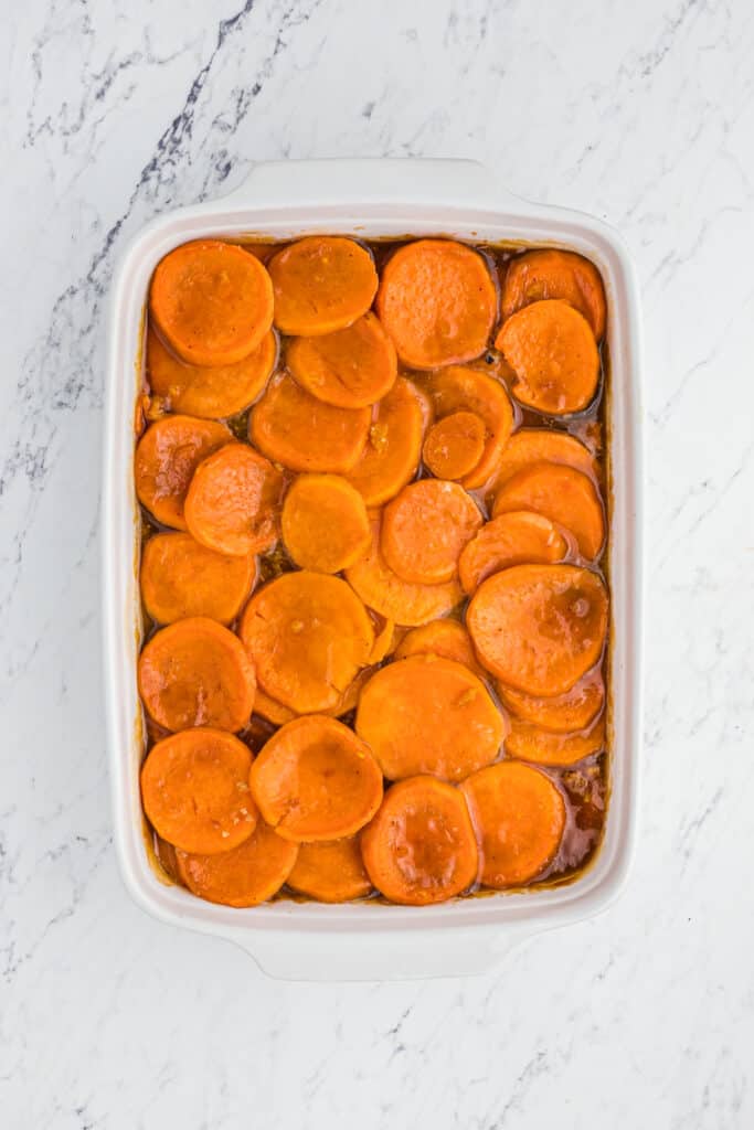 A white baking dish of sliced candy yam recipe in syrup.