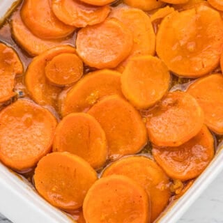 A white baking dish of sliced candied yams in syrup.