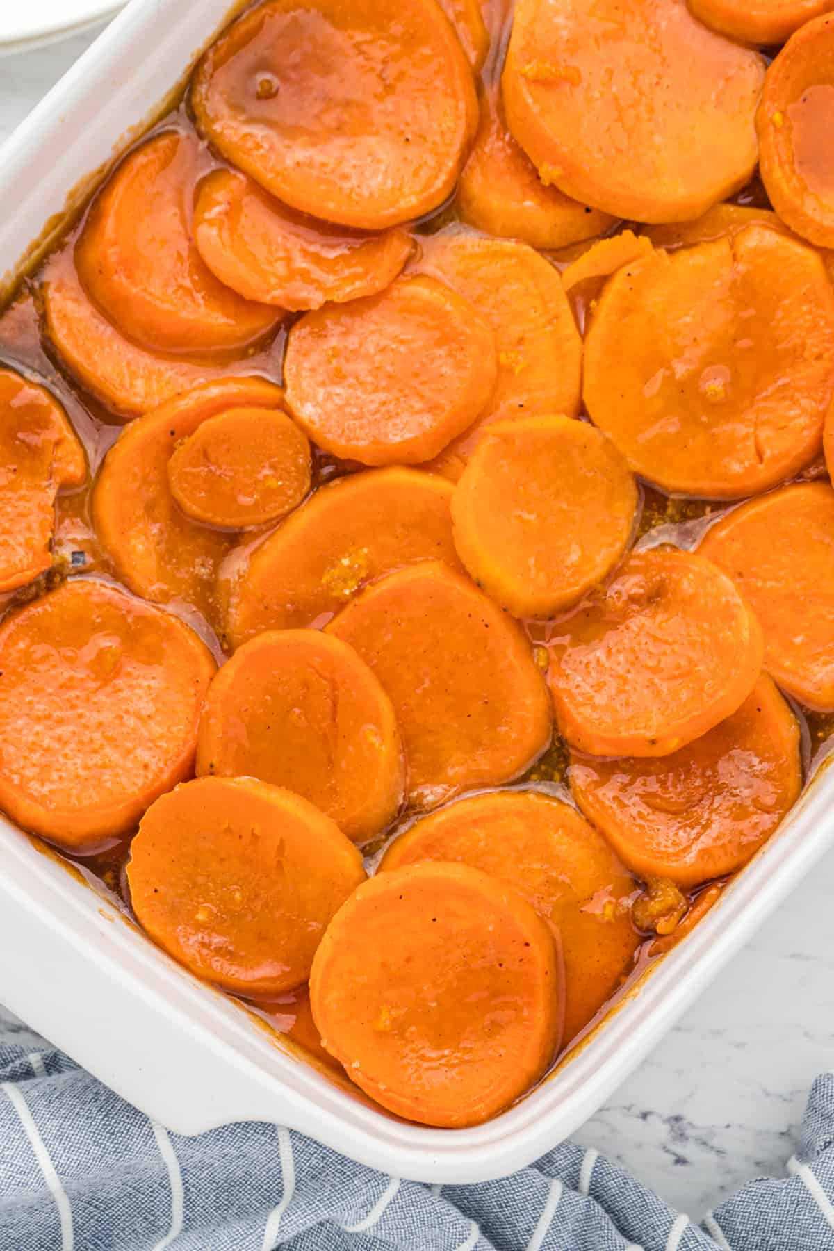 A white baking dish of sliced candied yams in syrup.