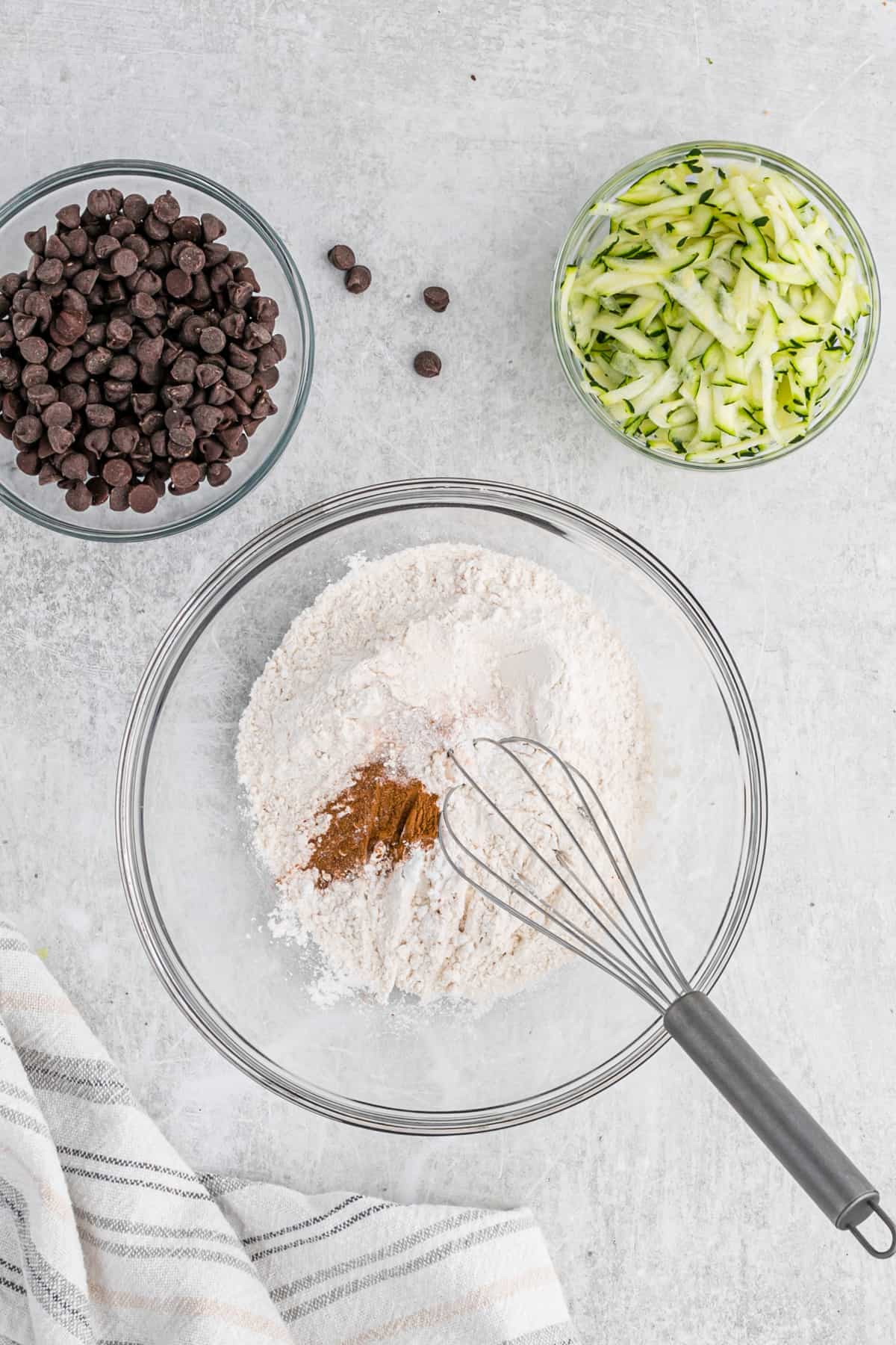 Small bowls with ingredients for chocolate chip zucchini bread on a counter.