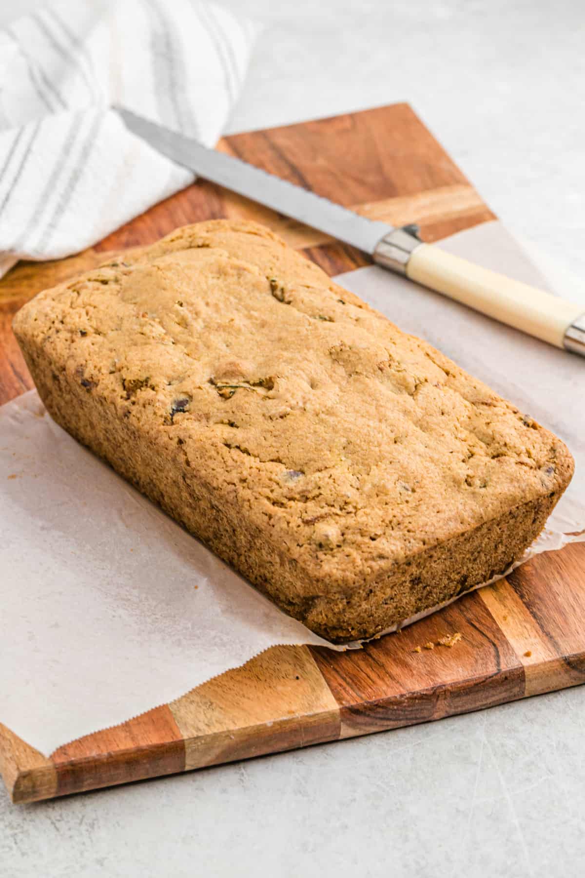 A fresh loaf of chocolate chip zucchini bread on a wooden cutting board.