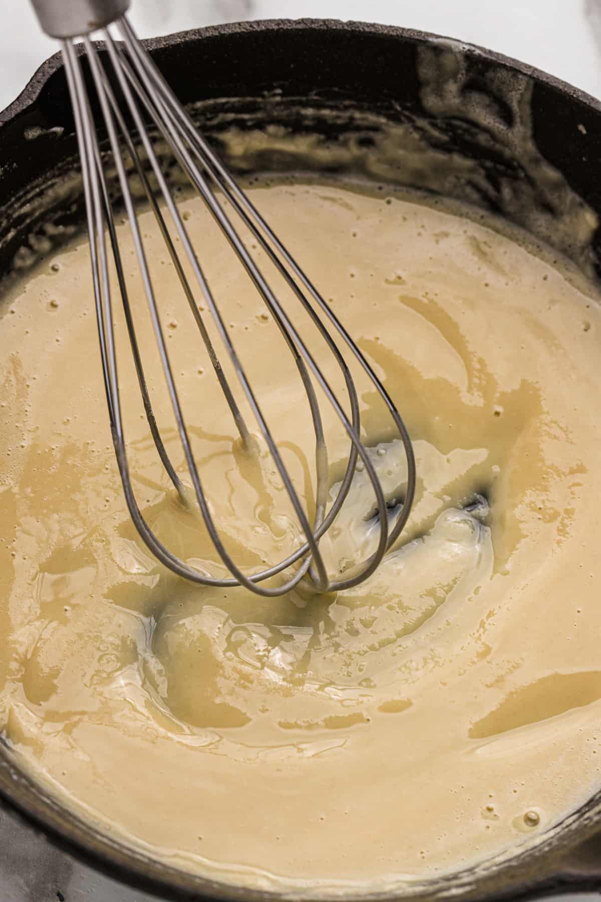 A whisk in a cast iron skillet of finished roux.