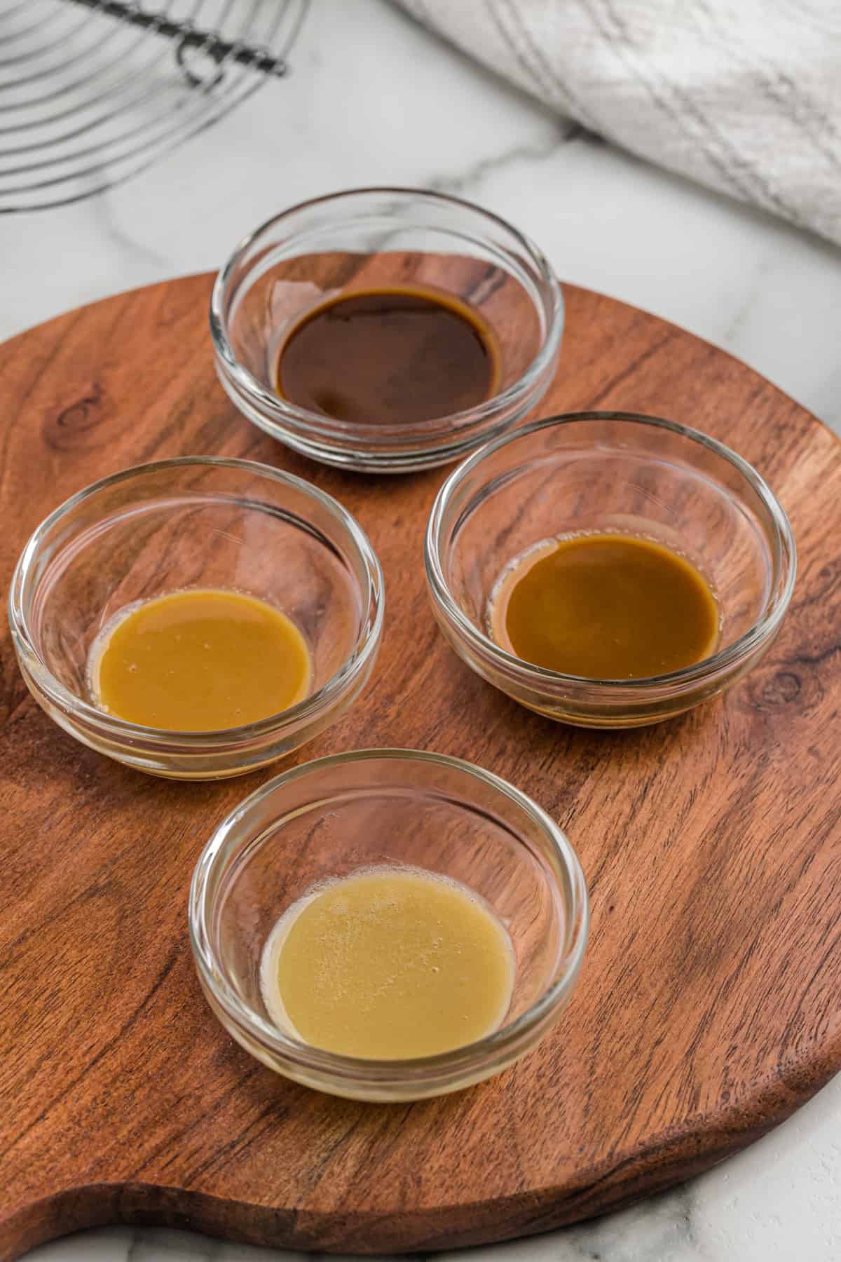 Roux in four stages of color in small bowls on a wood board.