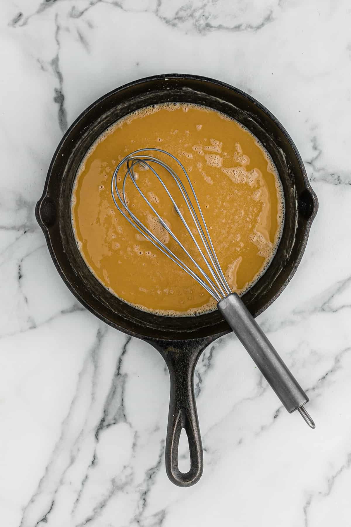 A whisk in a cast iron skillet of finished roux.