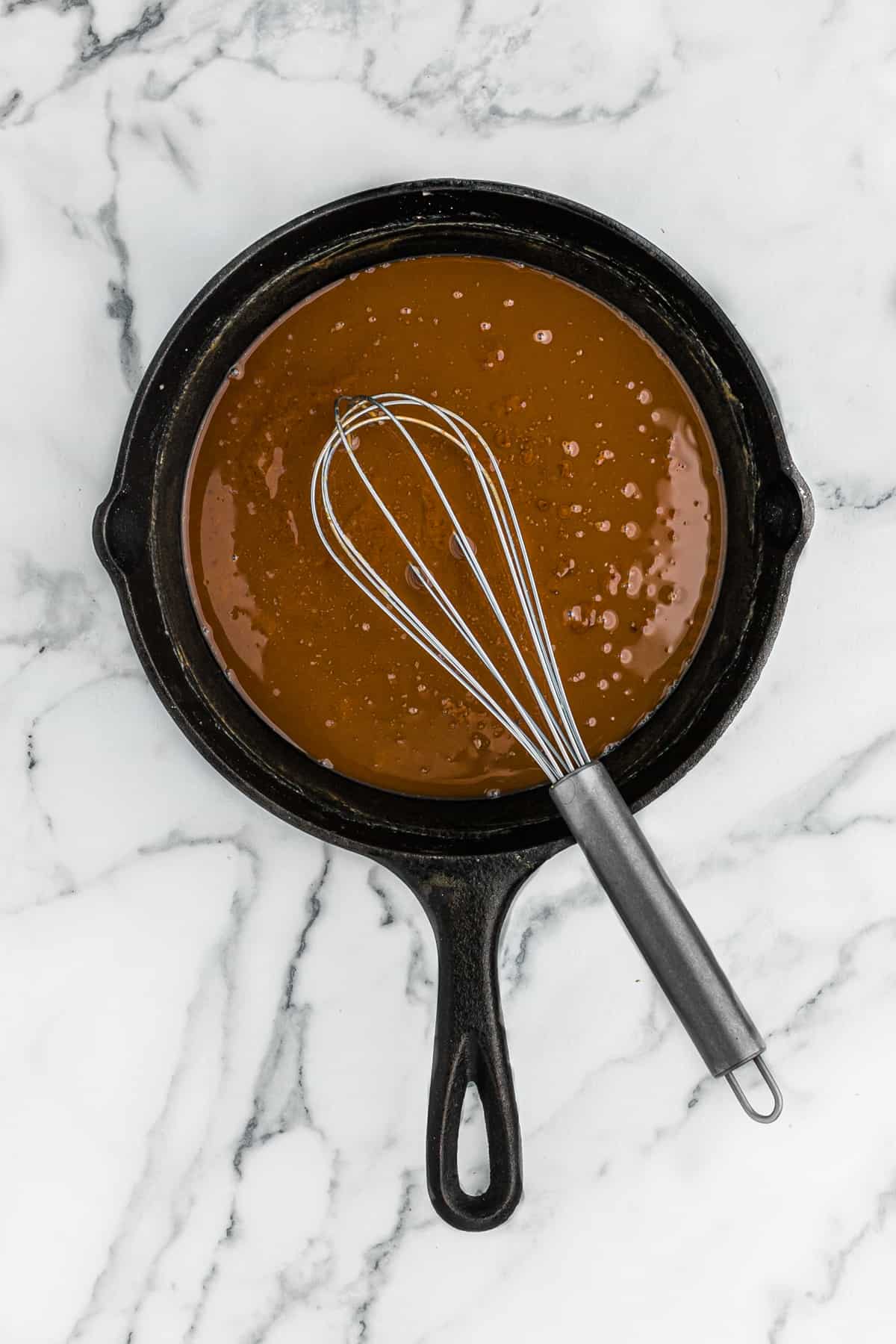 A whisk in a cast iron skillet of a finished sauce