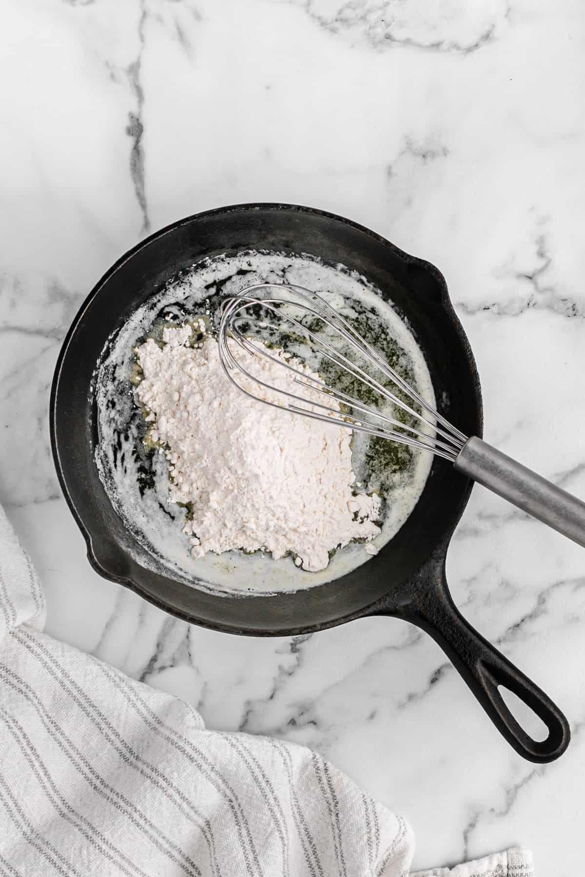 A whisk in a cast iron skillet of flour and melted butter.