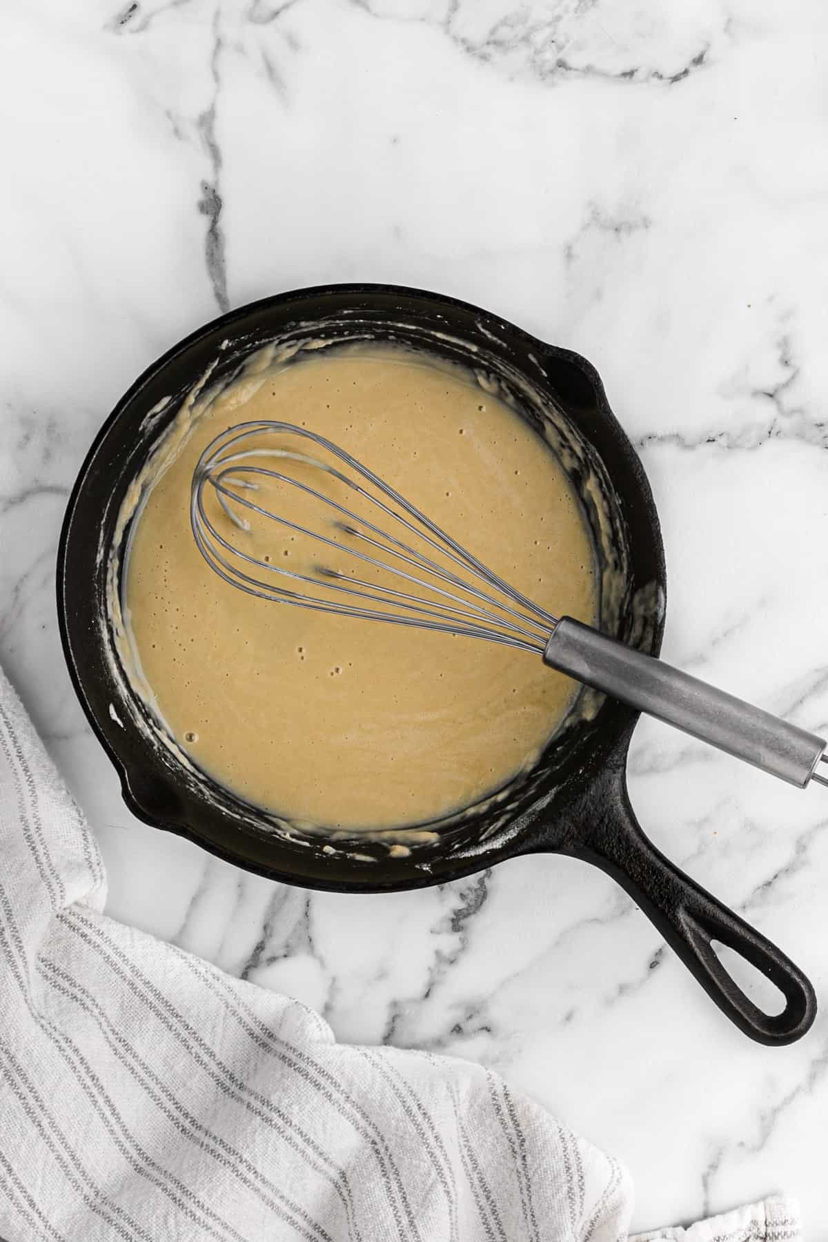 A whisk in a cast iron skillet of finished light sauce.
