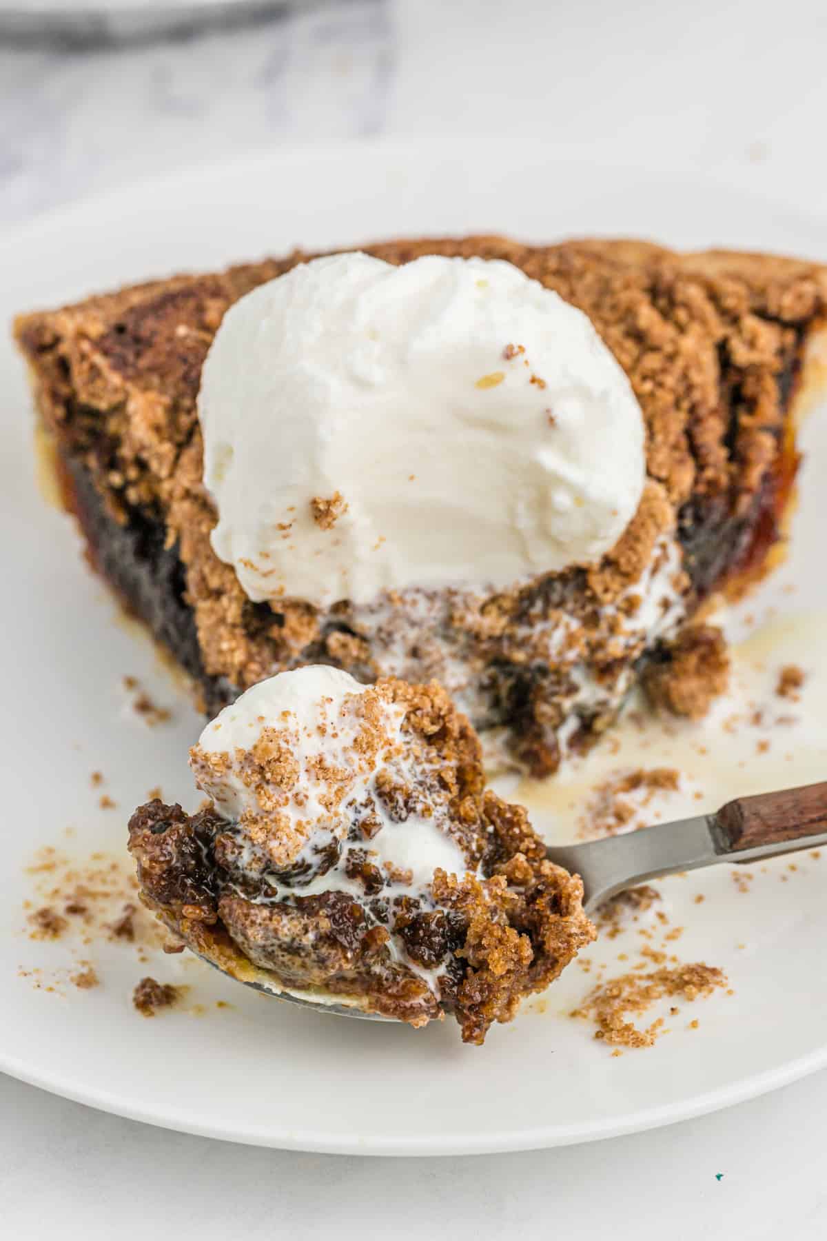 A spoon cutting into a slice of shoofly pie with vanilla ice cream on top.