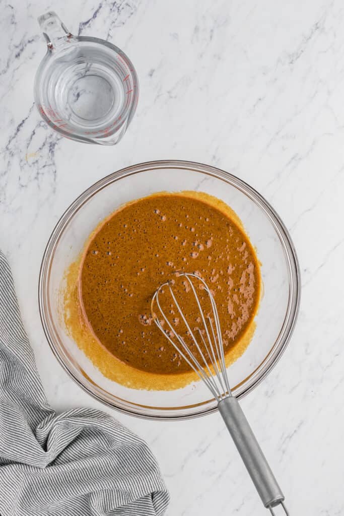 A whisk in a mixing bowl of brown sugar pie filling on white countertop