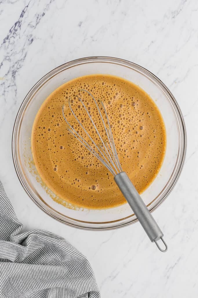 A whisk in a mixing bowl of shoofly filling on white countertop