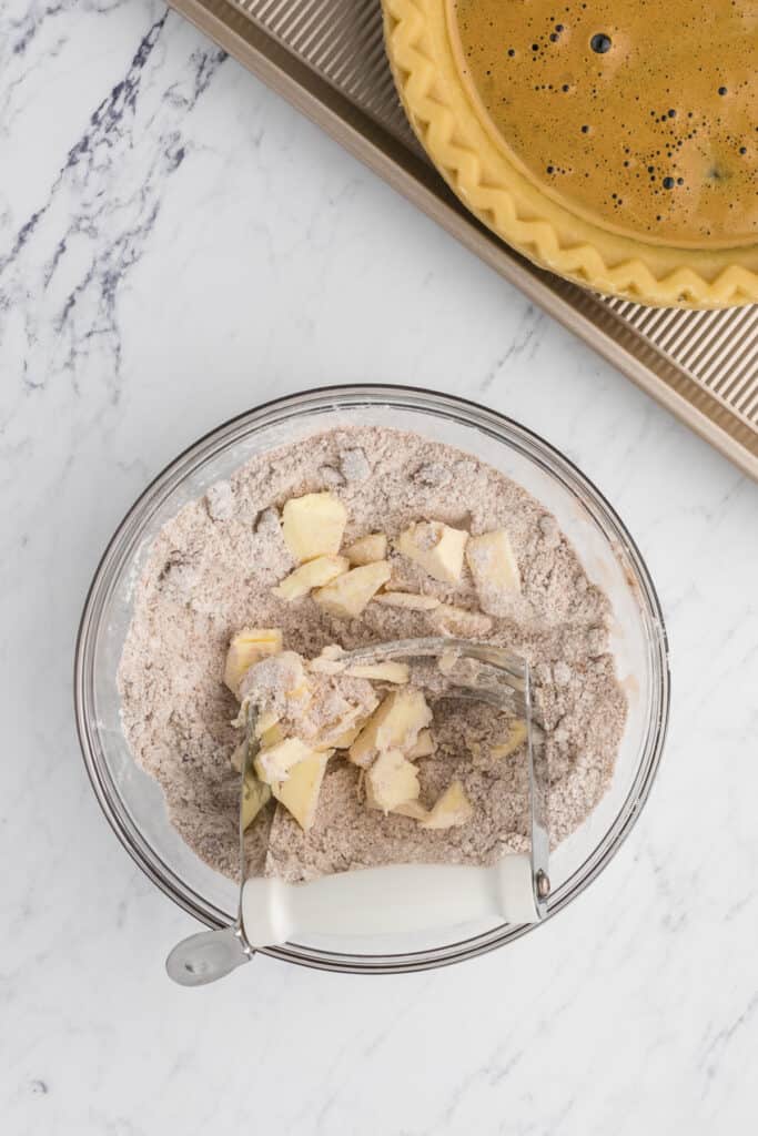 A pastry blender with butter and flour in a small glass mixing bowl.