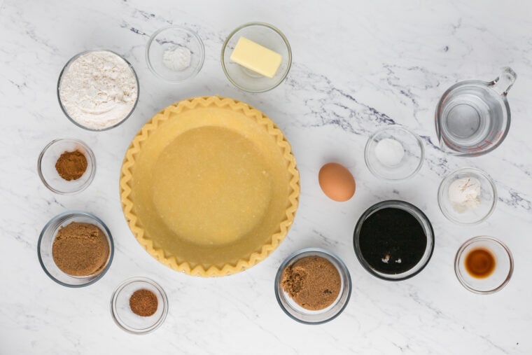 Molasses, sugar, eggs, butter, flour and other pie ingredients in glass bowls on white countertop