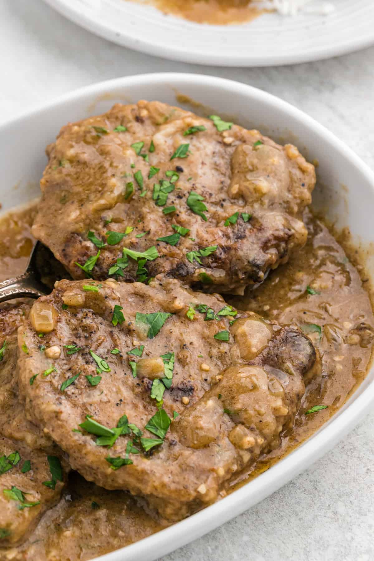 Round steak smothered in gravy in a white baking dish.