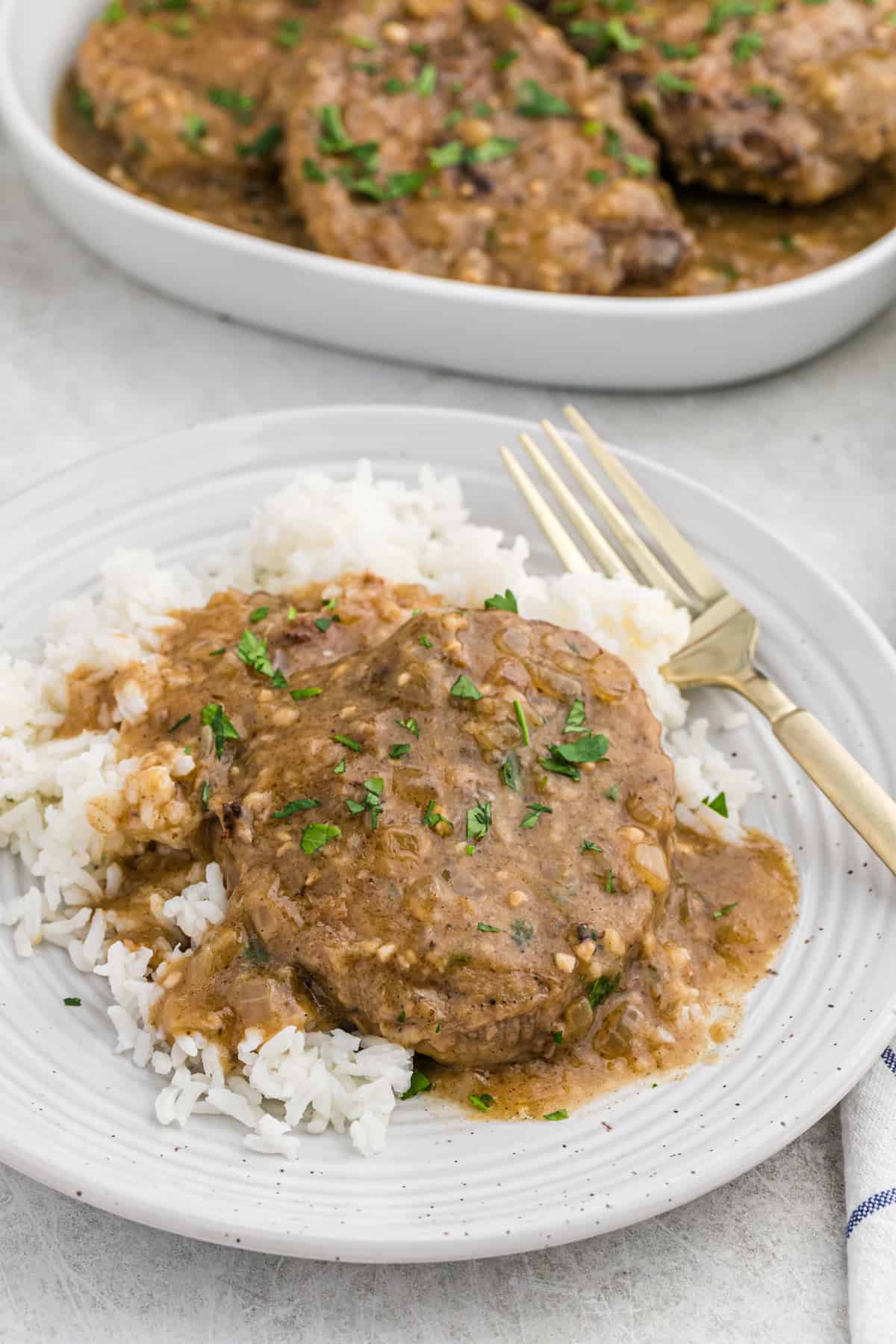 Smothered round steak over white rice with a gold fork on a dinner plate.