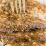A fork showing a cut slice of smothered round steak on a white plate.