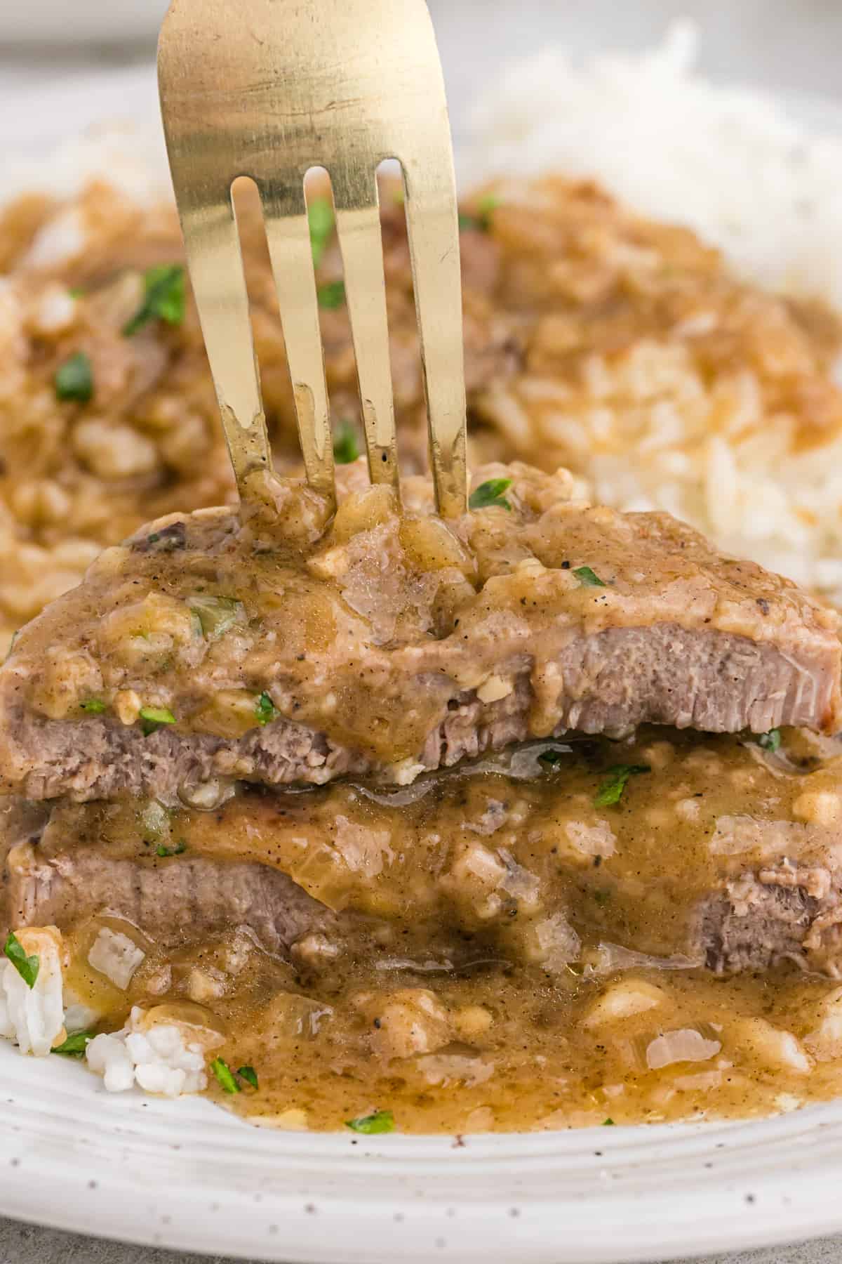 A fork showing a cut slice of smothered round steak on a white plate.