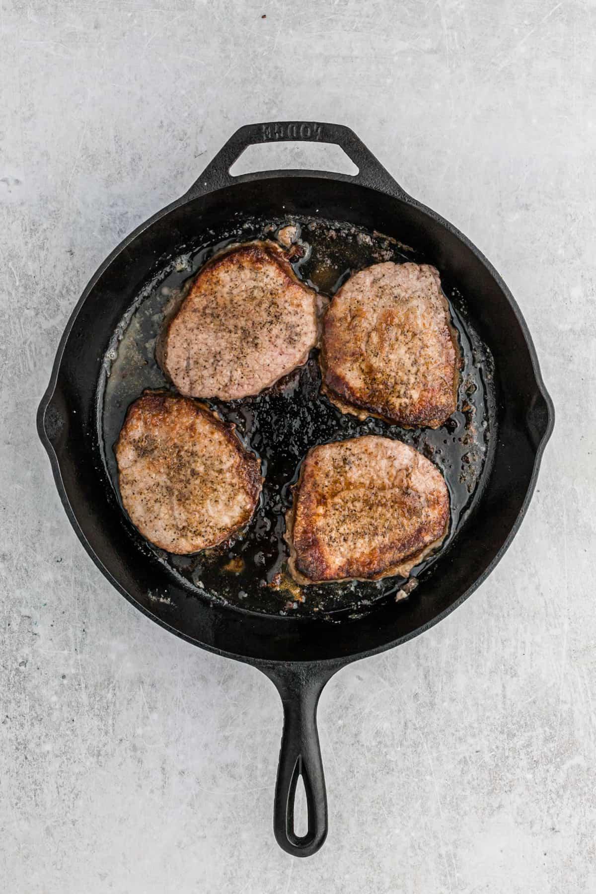 Round steaks sizzling in a large cast iron skillet.