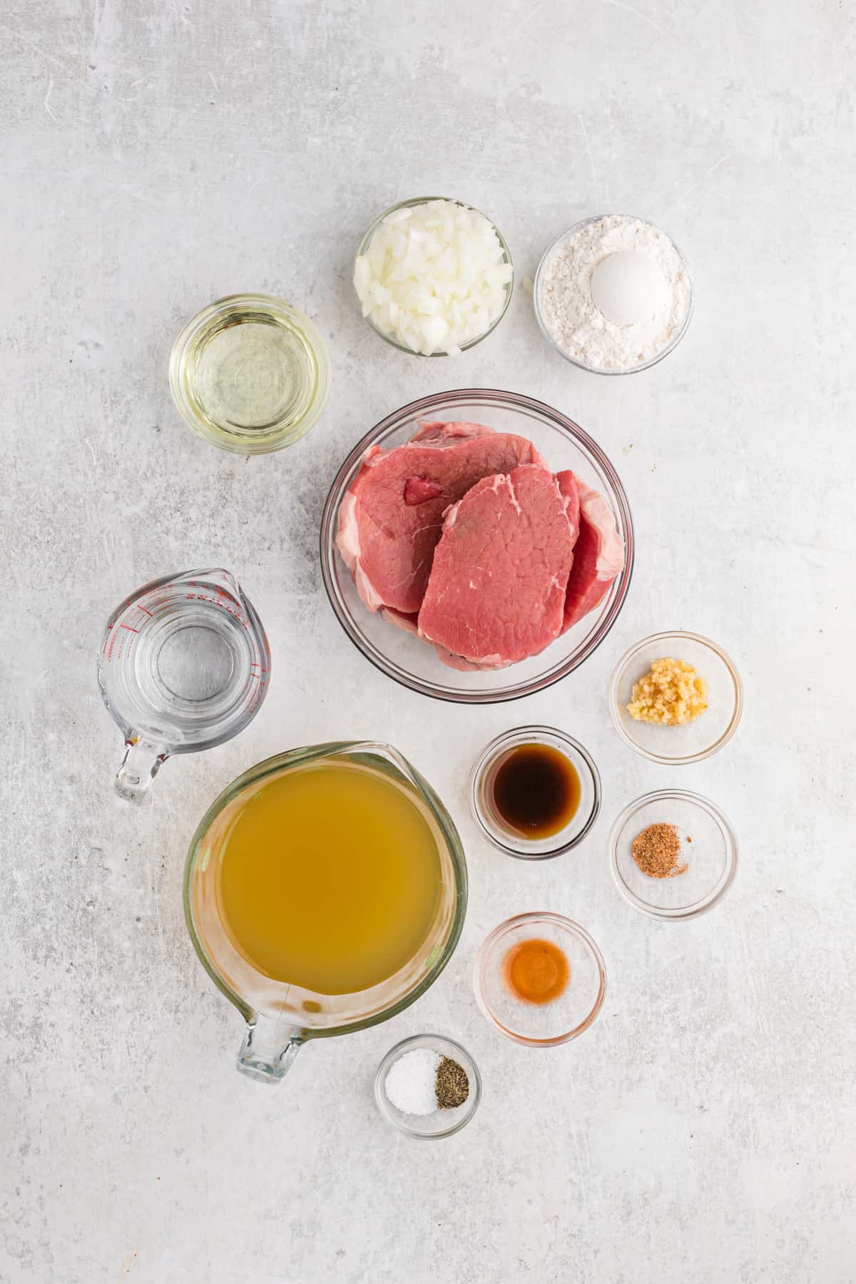 Ingredients to make smothered round steak in small bowls on a white surface.