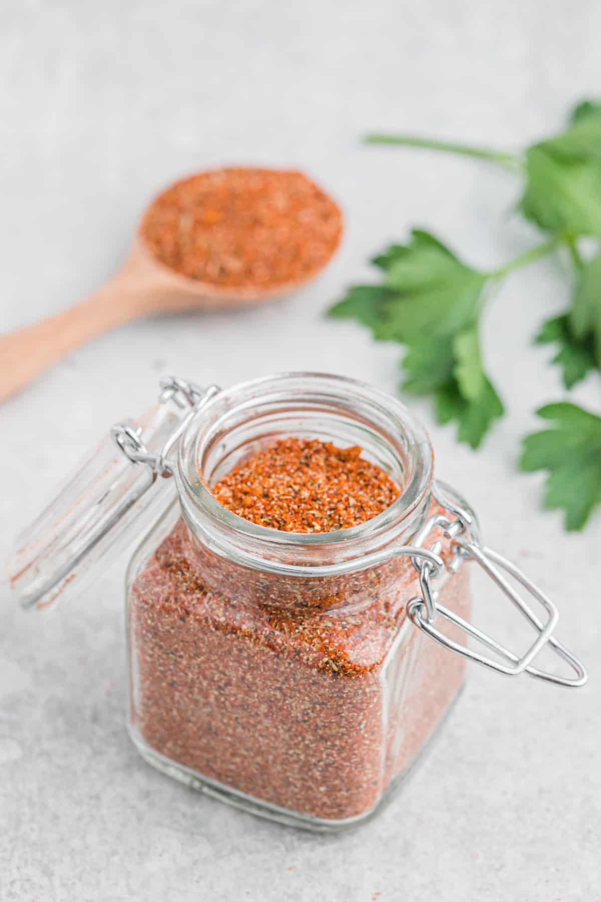 Homemade turkey rub seasoning in a small jar with a full wooden spoon on the table.