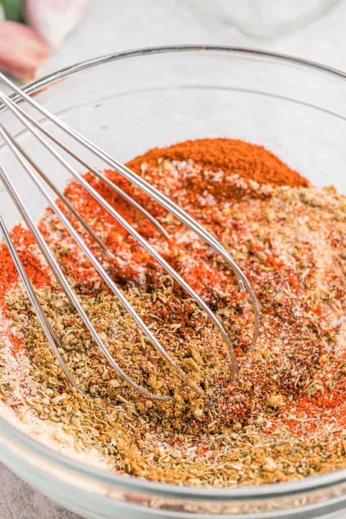 A whisk in a bowl of spices to make homemade turkey rub seasoning.