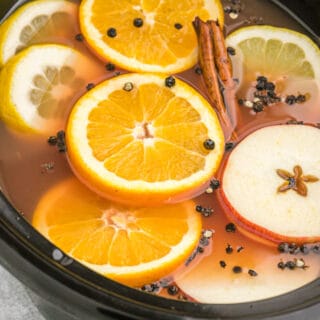 A crock pot filled with wassail, sliced fruit, and whole spices.