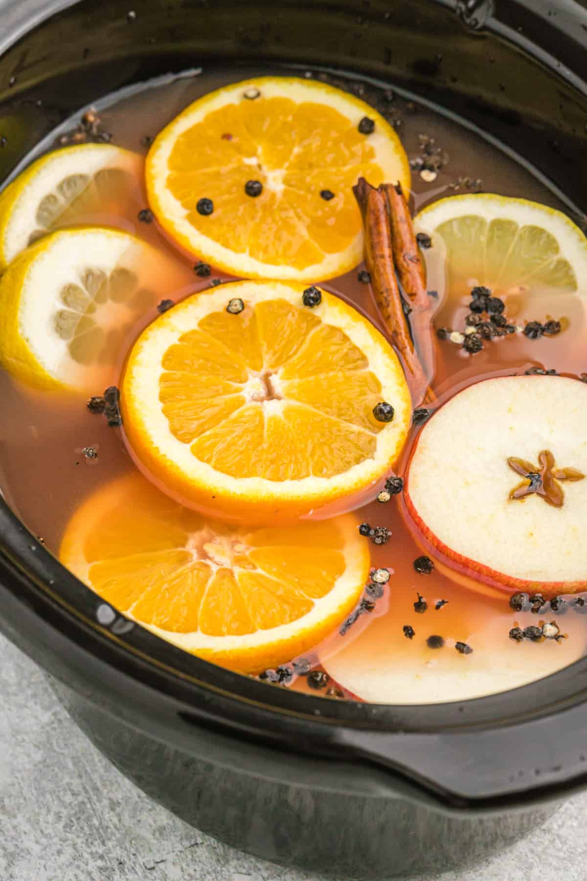 A crock pot filled with wassail, sliced fruit, and whole spices.