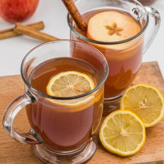 Two mugs of wassail with slices of orange and apple floating on top.