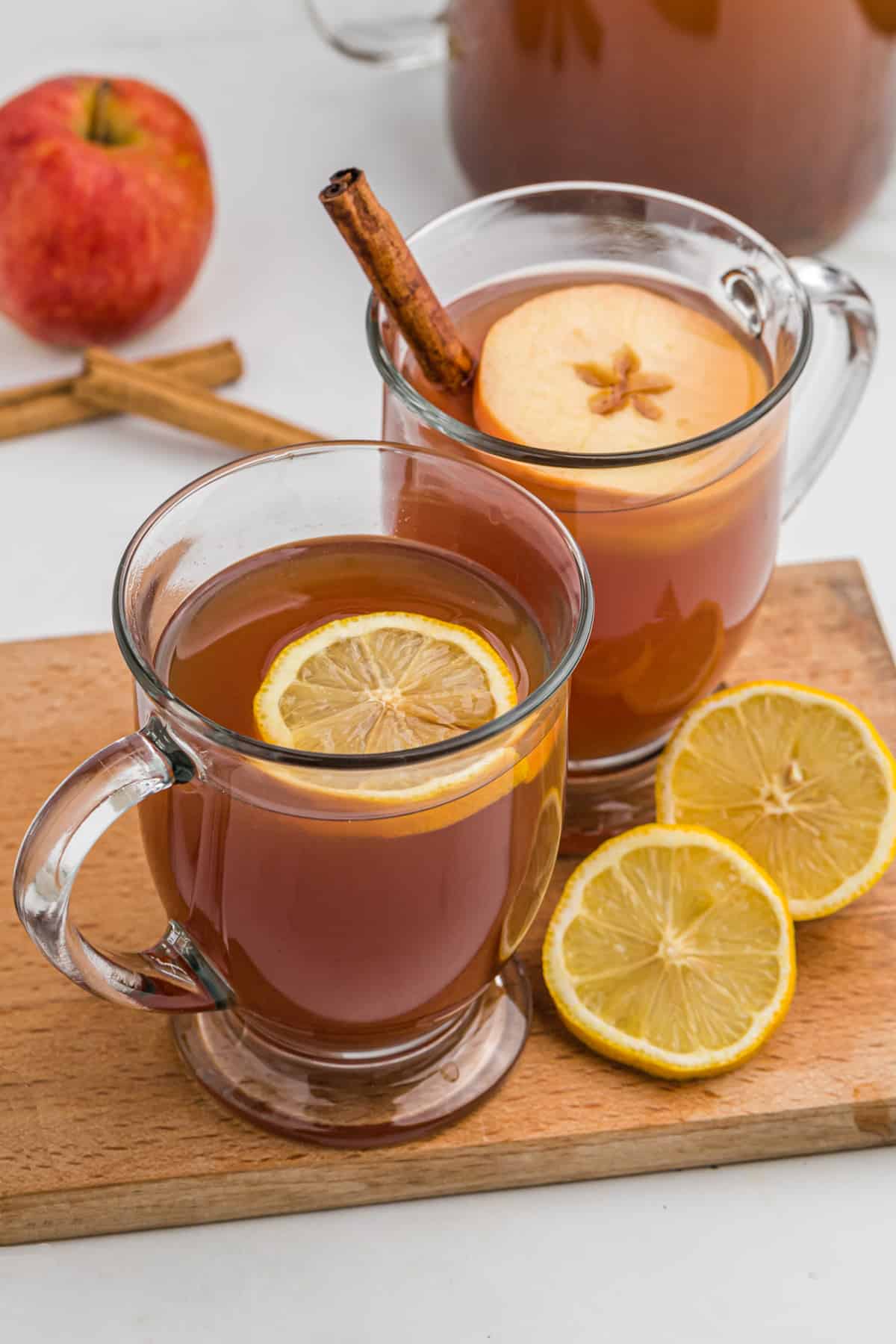 Two mugs of wassail with slices of orange and apple floating on top.