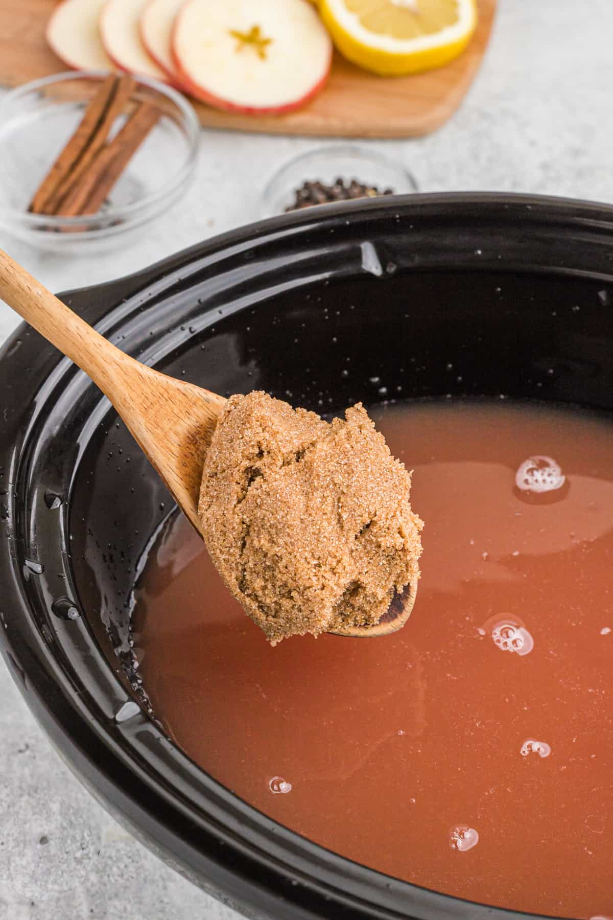 A wooden spoon adding brown sugar to a crockpot of wassail.