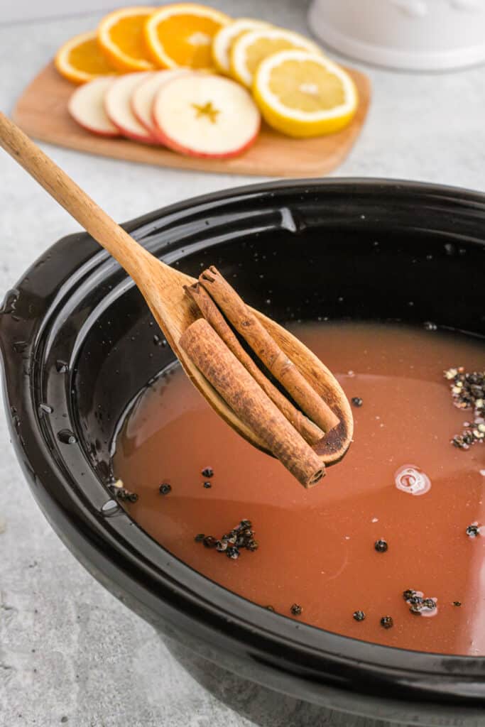 A wooden spoon adding whole cinnamon sticks into wassail.
