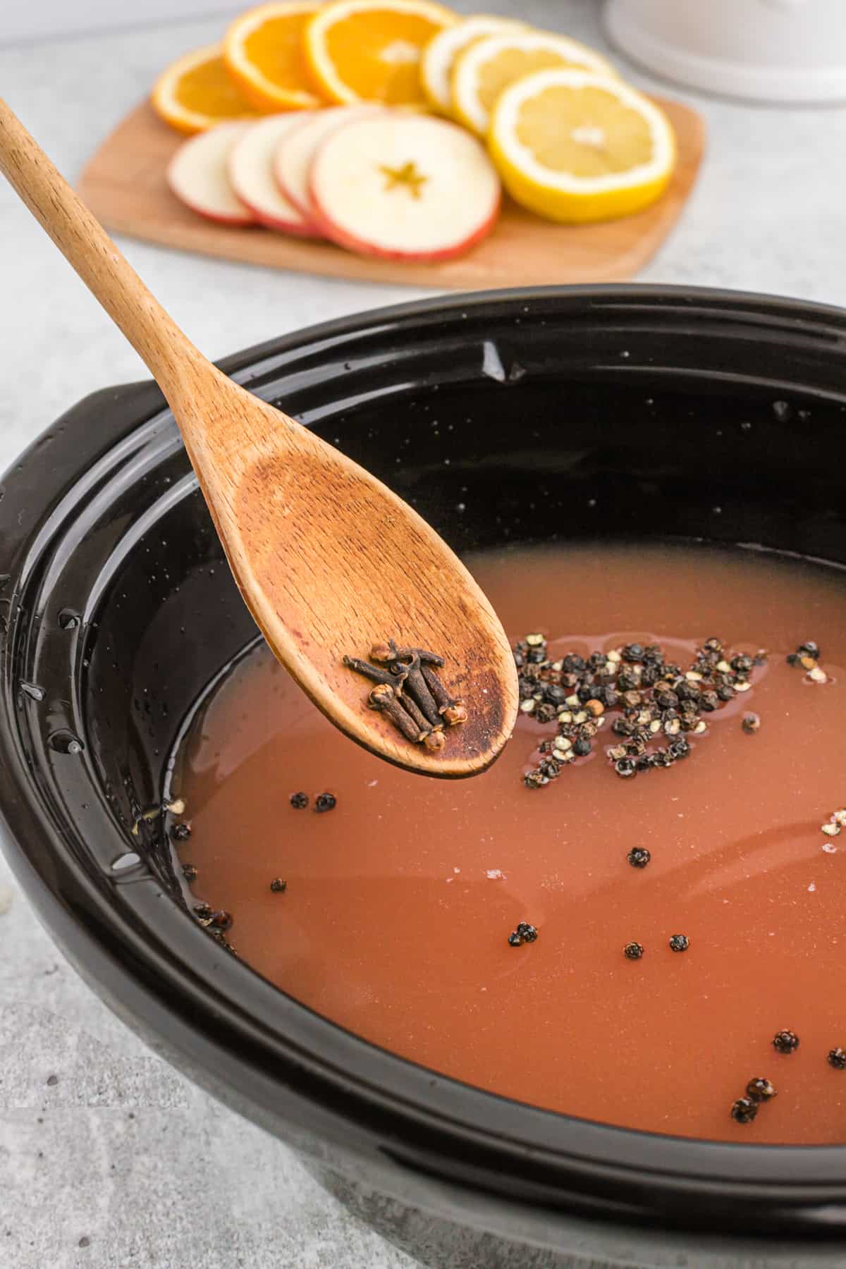 A wooden spoon dropping whole cloves into wassail.