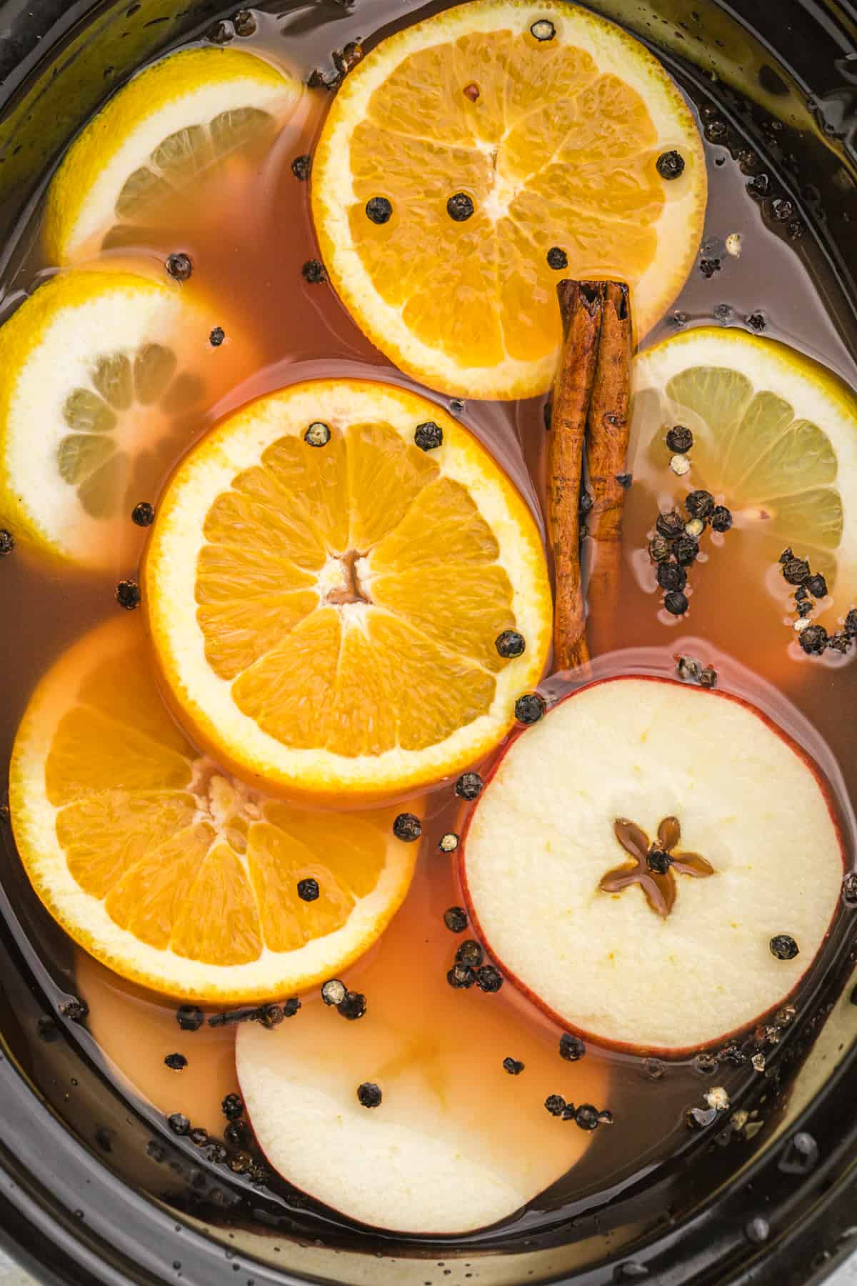 A crock pot filled with wassail, sliced fruit, and whole spices.