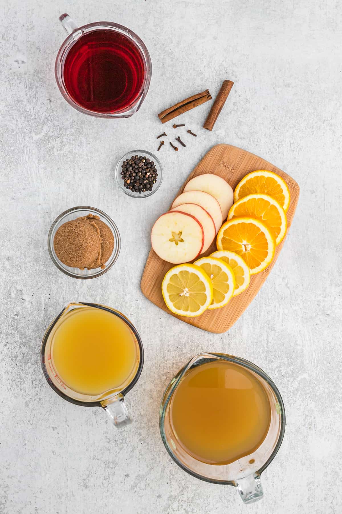 Ingredients to make wassail in bowls and measuring cups on a white counter.