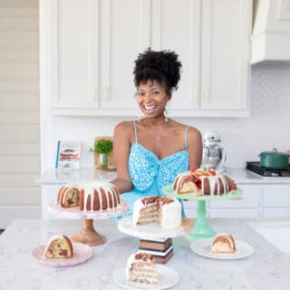 Jocelyn Delk Adams standing with three cakes on cake stands and smiling