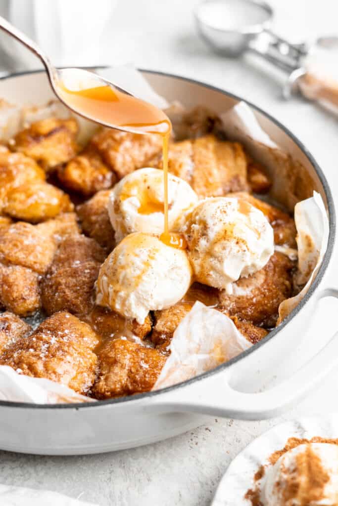 apple dumplings baked in a pan with ice cream on top being topped with a drizzle of caramel