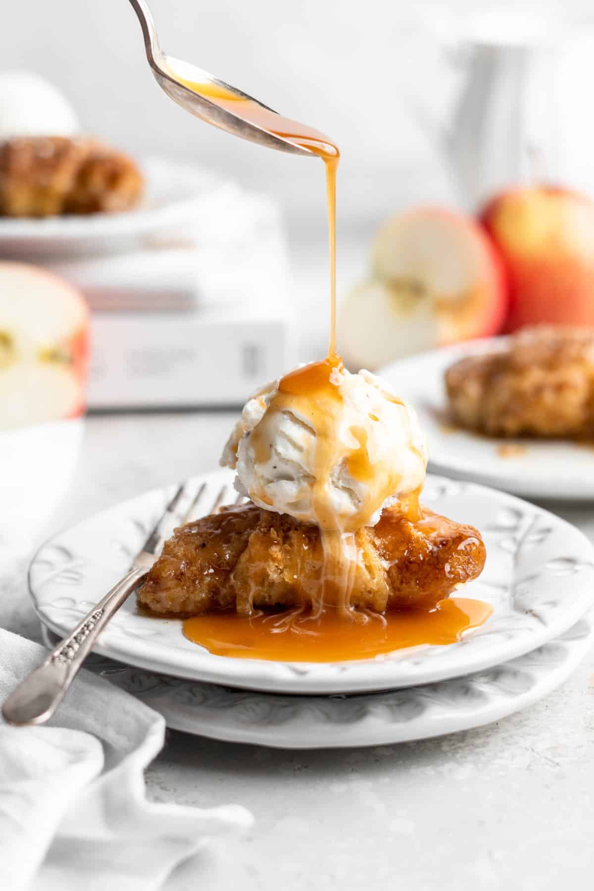 apple dumpling on a white plate topped with ice cream and caramel being drizzled on top