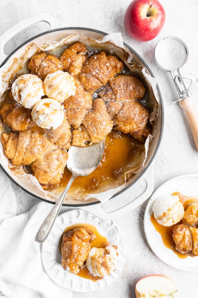 overhead of apple dumplings in a pan being served on small white plates with ice cream