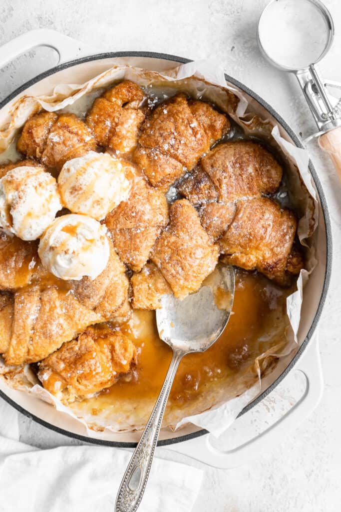 apple dumplings in a pan with ice cream and a spoon for serving