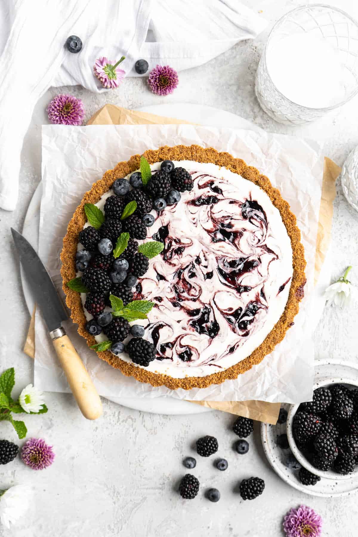 A no bake lemonade pie tart against a white background with blackberries and blueberries in a white glass bowl