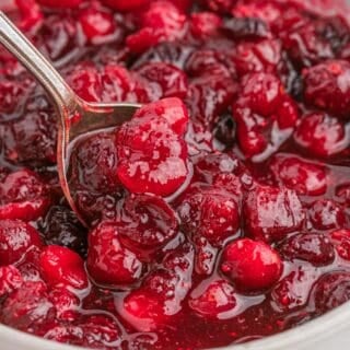 A spoon in a white bowl of whole berry cranberry sauce.