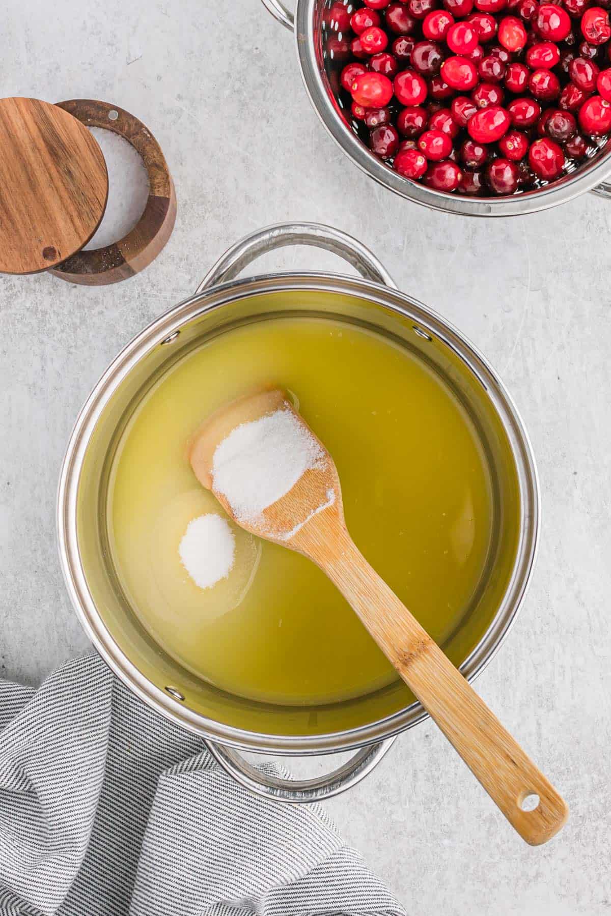 A wooden spoon in a pot of sugar and juice to make cranberry orange sauce.