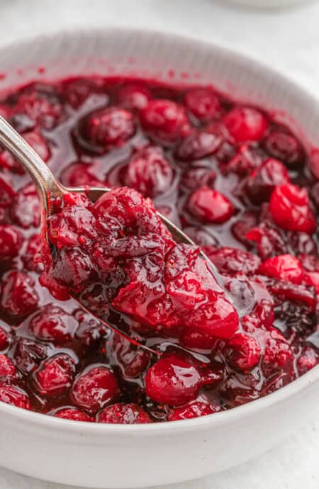 A spoon in a white bowl of whole berry cranberry sauce.