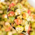 A close up of okra and tomatoes on a spoon