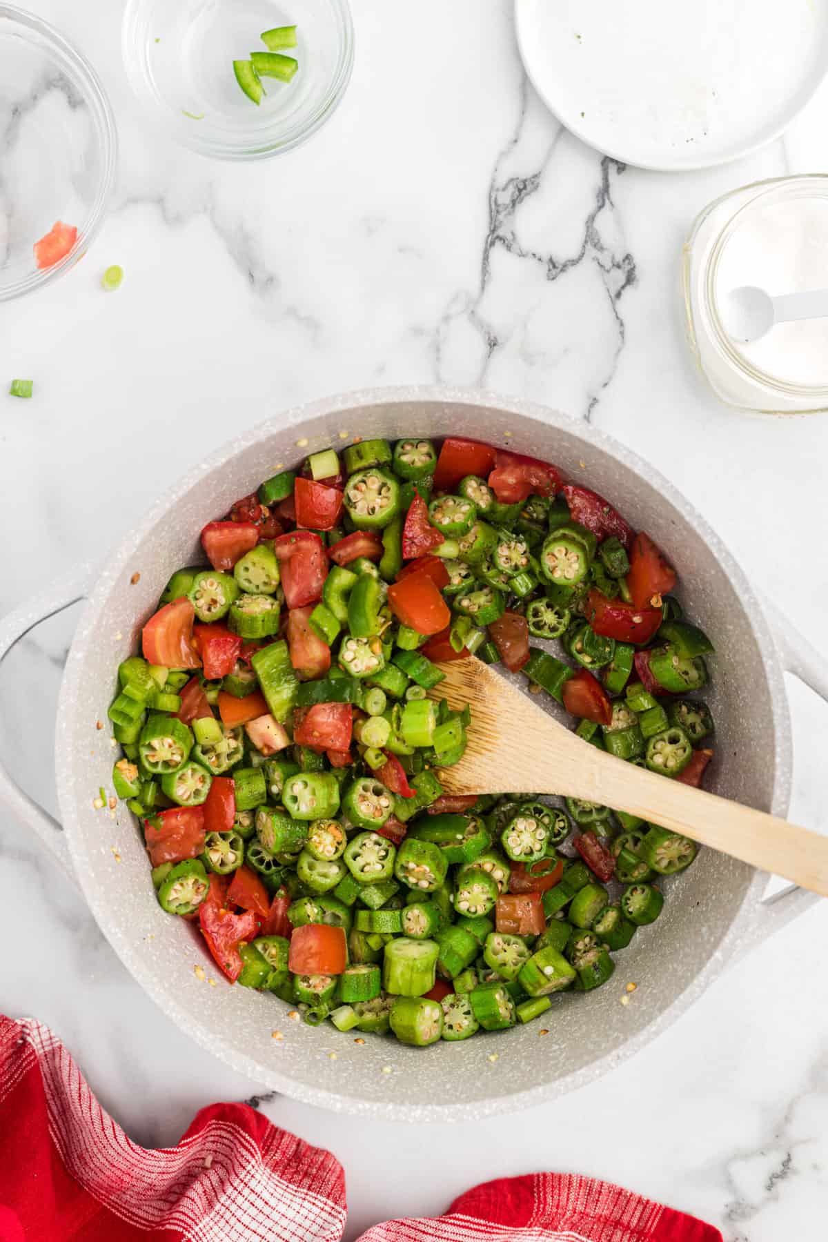okra and tomatoes in a large pot with a wooden spoon