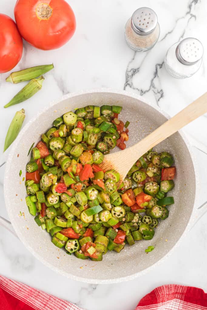 okra and tomatoes in a large pot with a wooden spoon