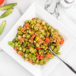 large white square dish filled with okra and tomatoes with a spoon