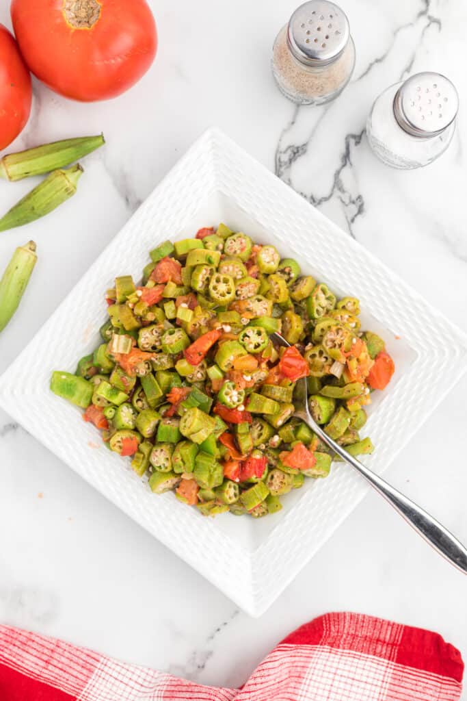 large white square dish filled with okra and tomatoes with a spoon
