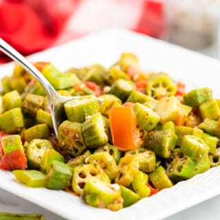 close up of white dish of okra and tomatoes with a spoon